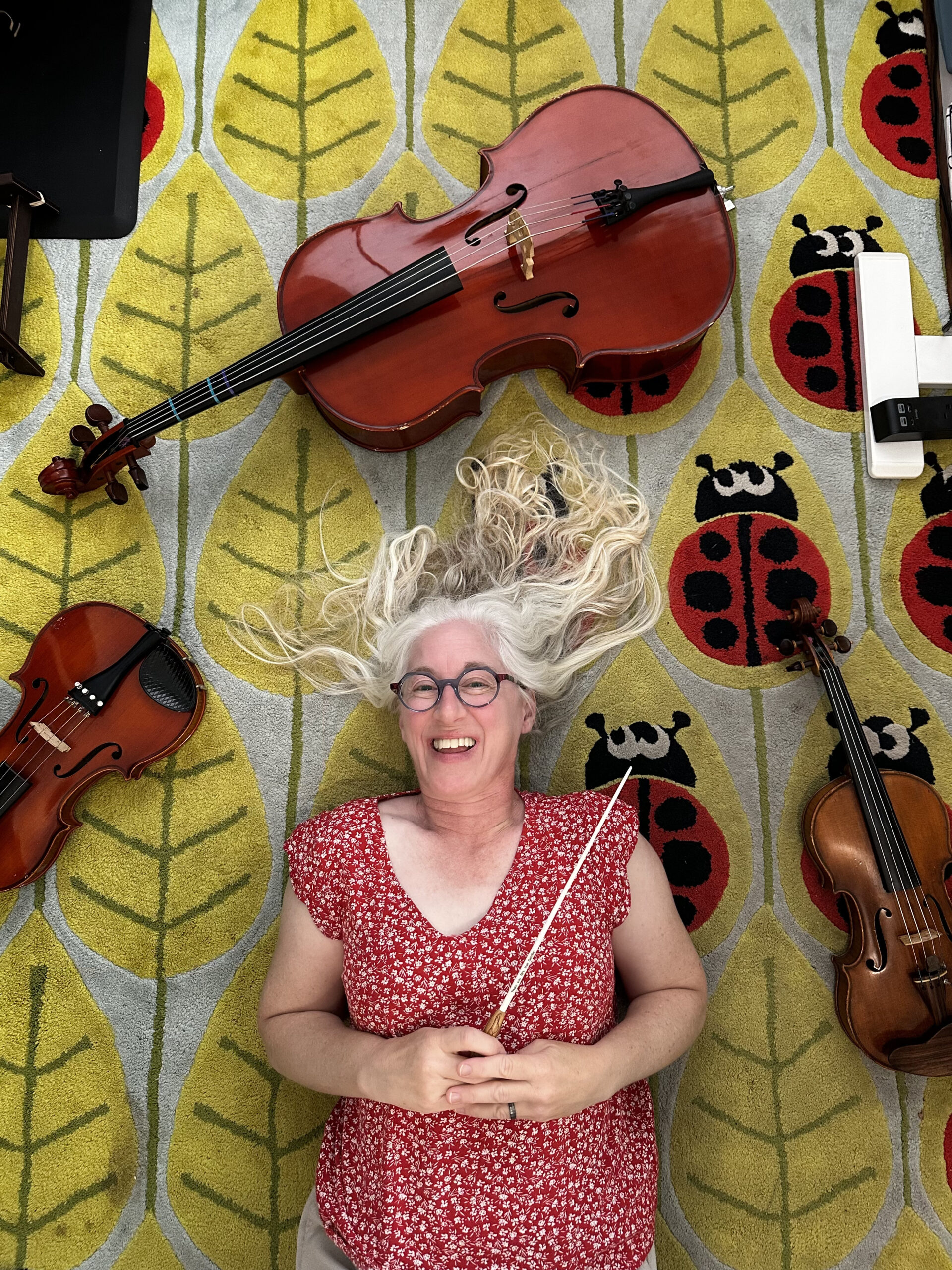 Camellia juniors conductor Reylynn Imai has long white hair and lays on a ladybug rug with violins and cellos around her.